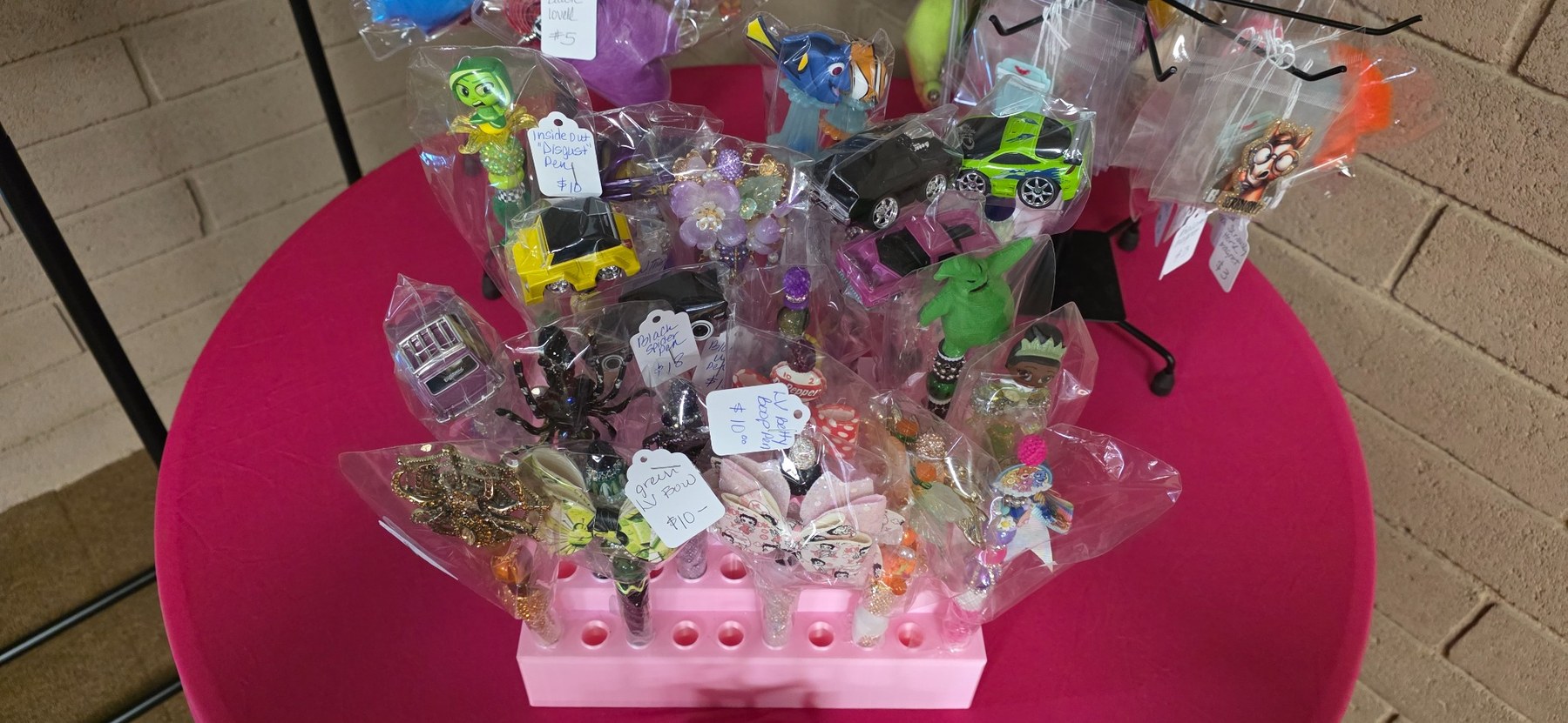 Dawn Lovell's colorful beaded pens and character accessories displayed on a pink table