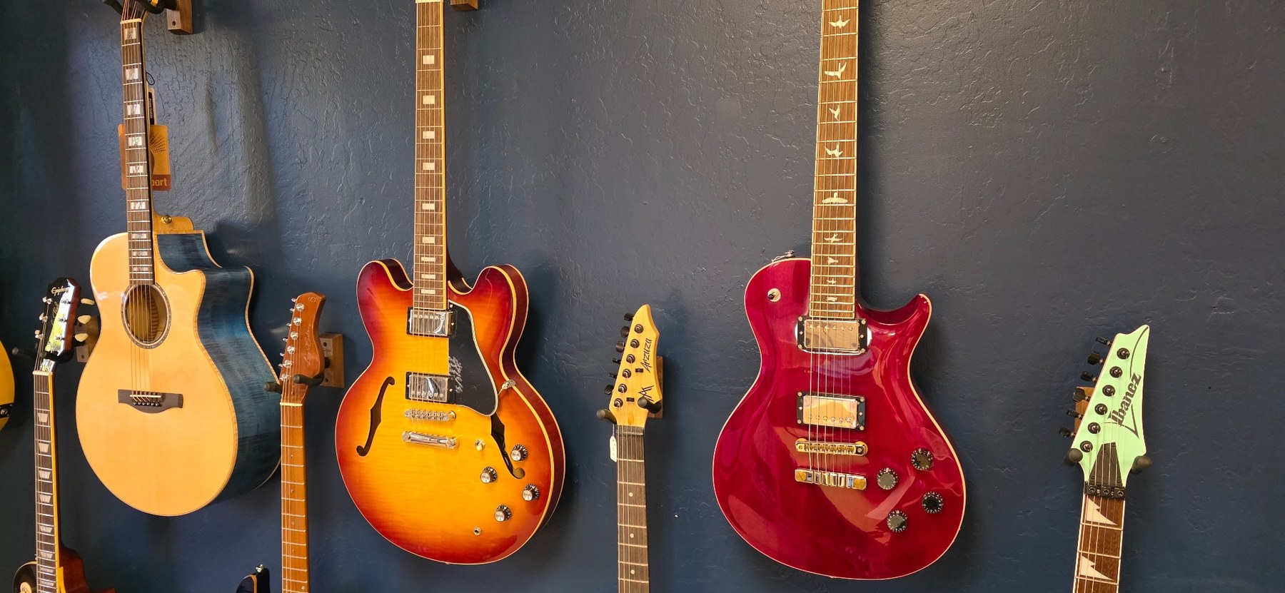 A closer view of acoustic, hollow-body and electric guitars hanging on the store's dark blue wall