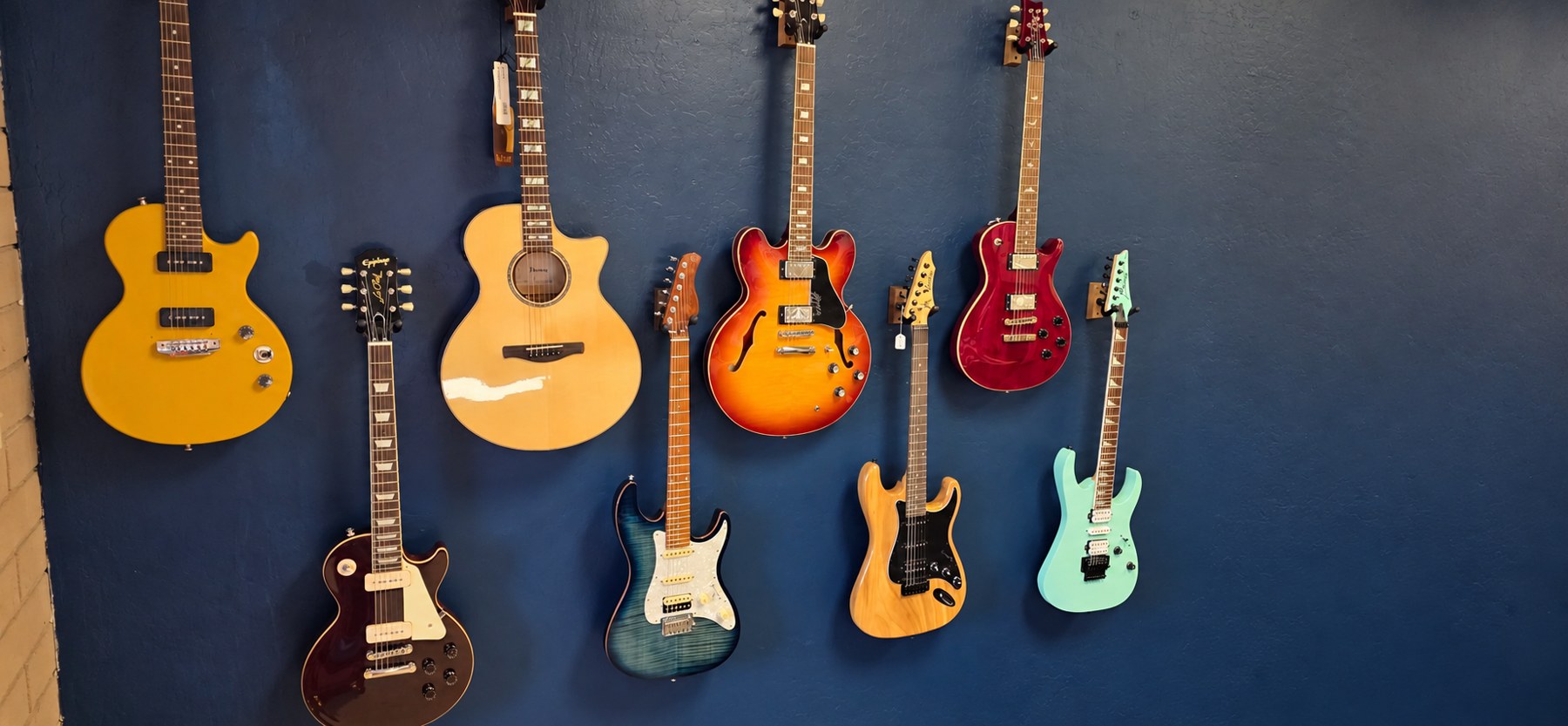 Acoustic and electric guitars hanging on the dark blue wall at Cottonwood Makers Mart